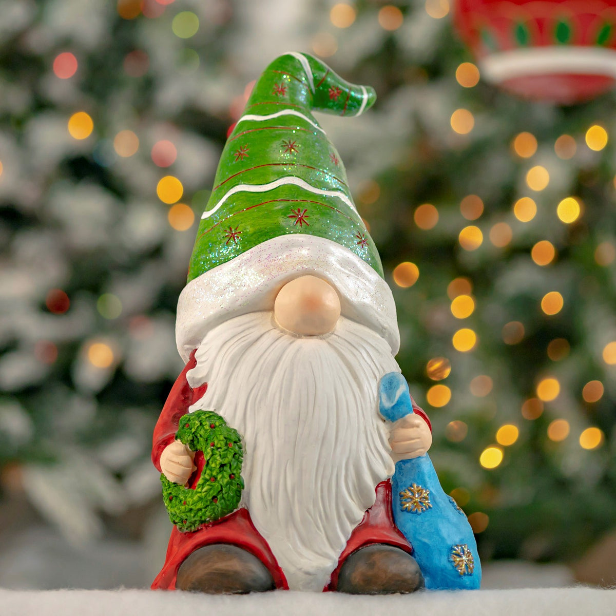 A colorful Christmas gnome statue with a green hat and wreath sits against a softly lit tree.