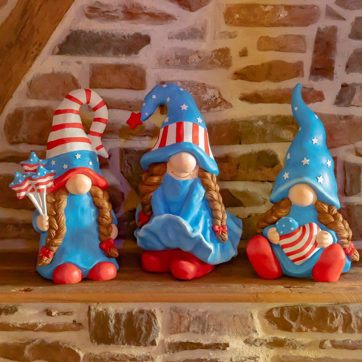 Three patriotic lady gnomes sit on a wooden ledge against a stone wall.