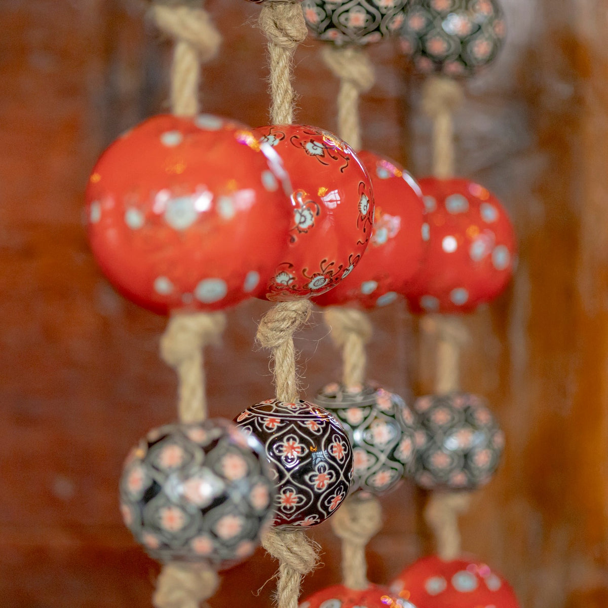 Close-up of red porcelain balls with pale floral motifs and dark patterned balls threaded on rough cord.