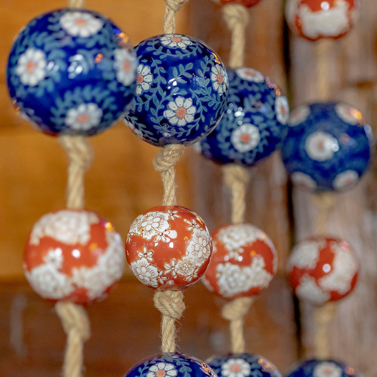 Close-up of glossy blue and burnt-orange balls with white floral patterns tied along twine.