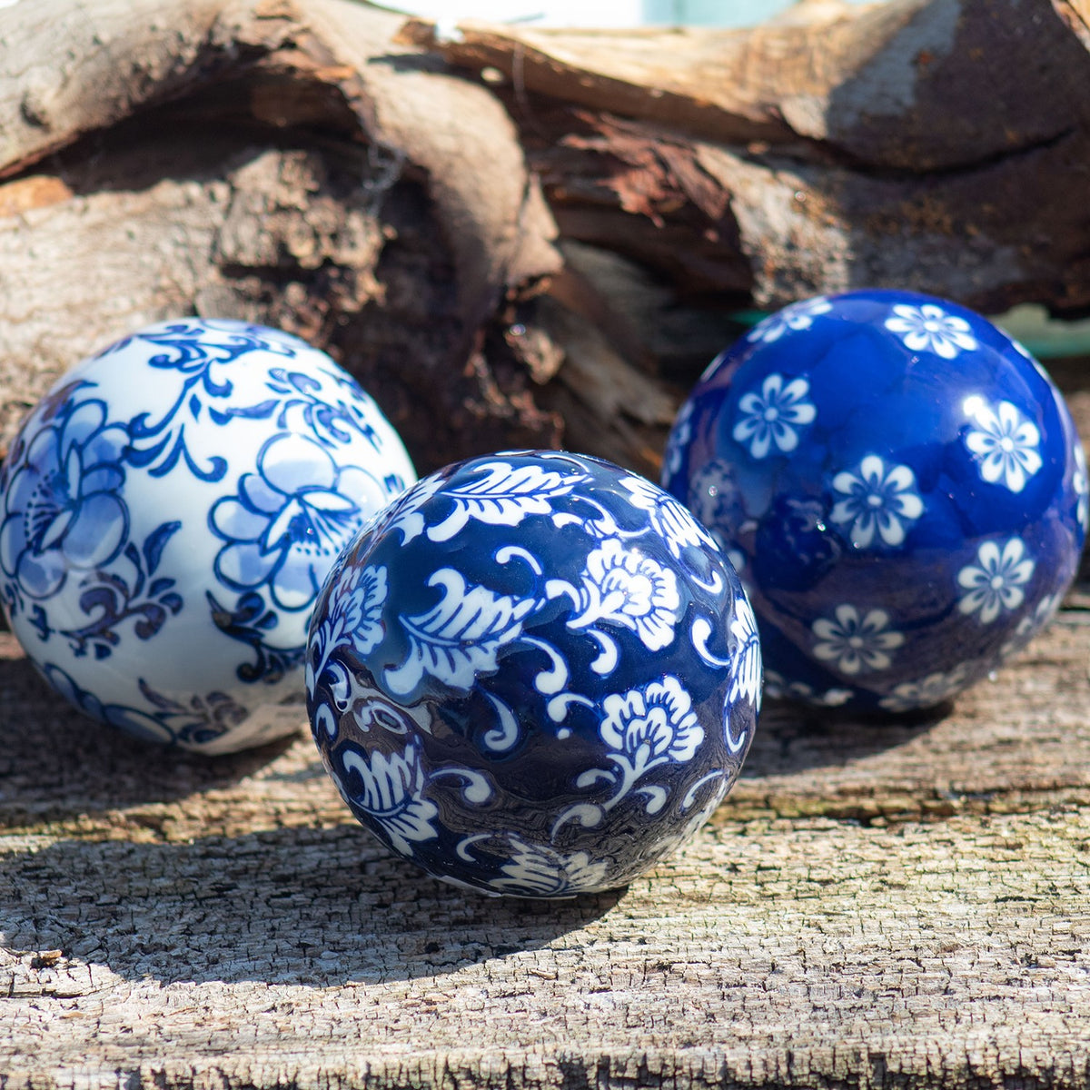 Three blue-and-white patterned ceramic balls arranged on weathered wood beside a piece of driftwood.