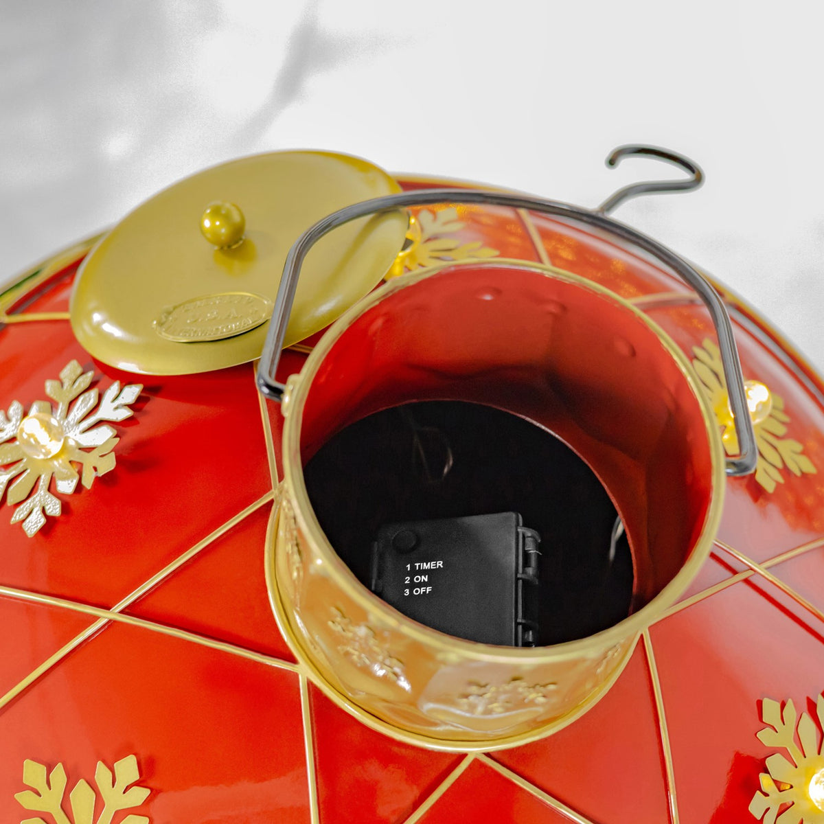 The ornament is open, showing its dark interior, battery compartment, metal handle, and detached lid.