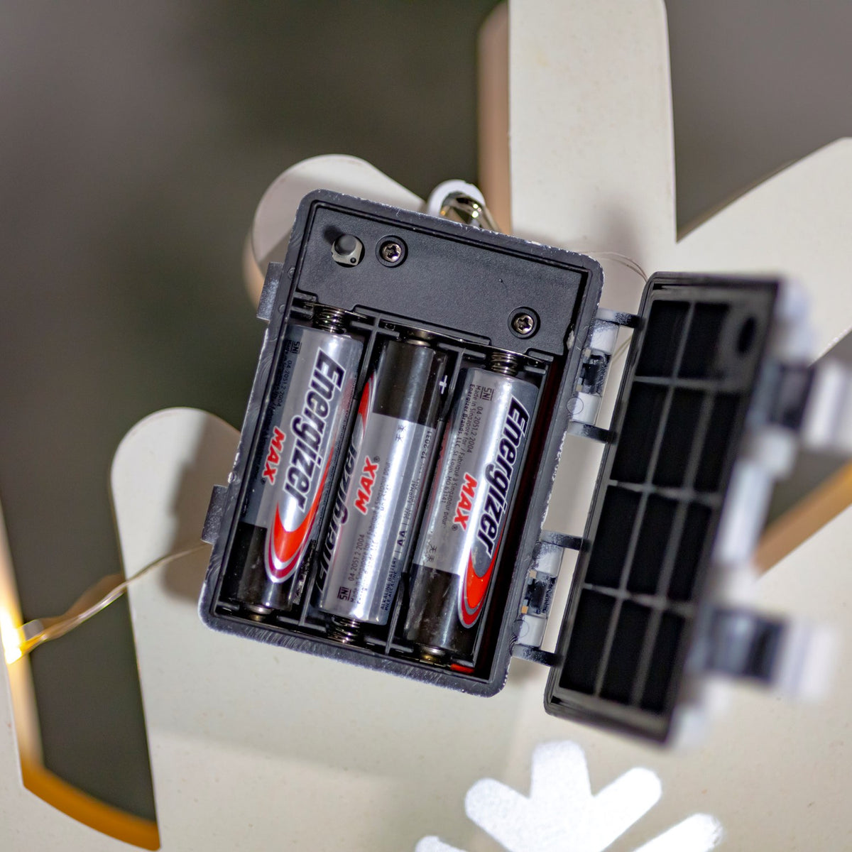 Open battery compartment with three batteries attached to the back of a white snowflake decoration.