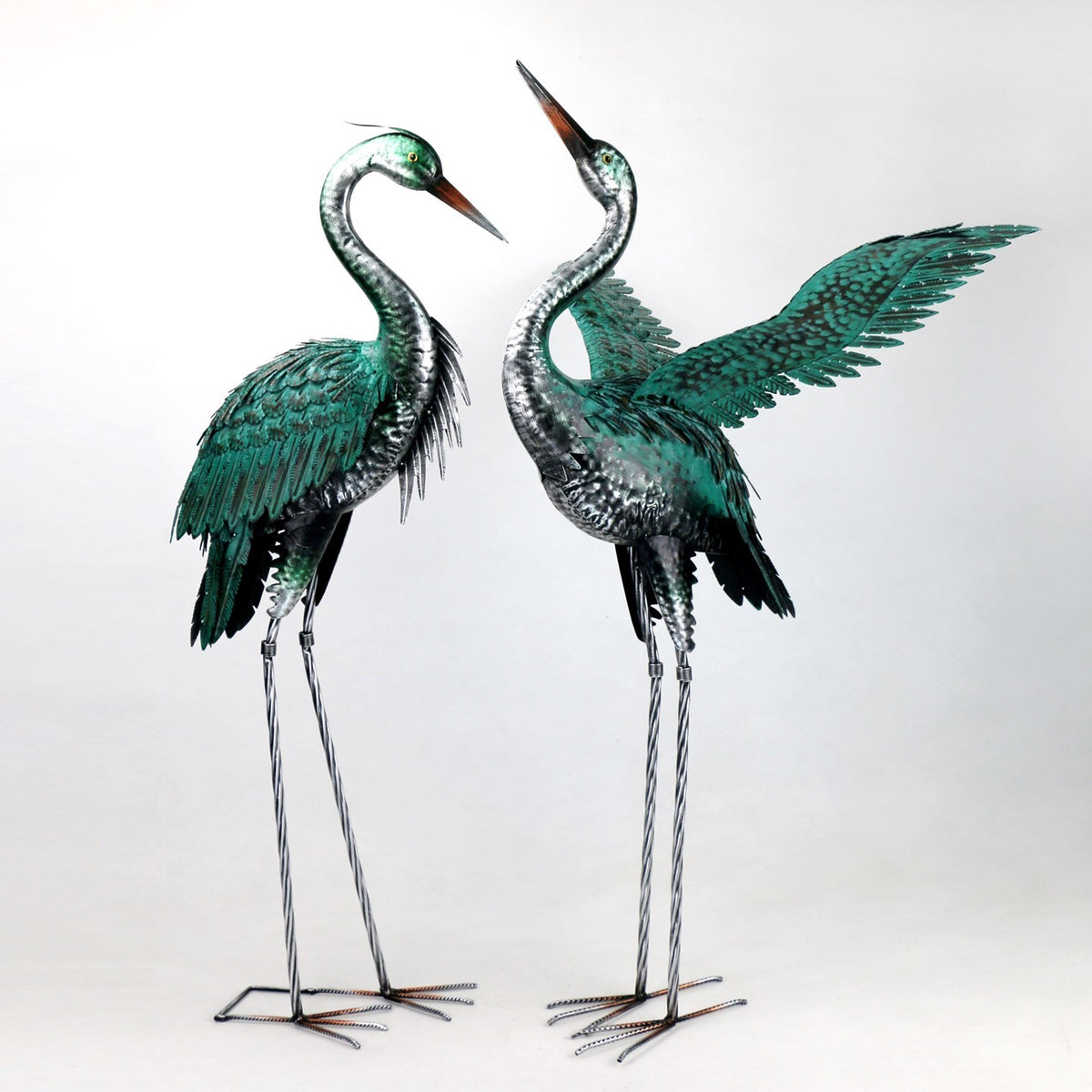 Two metal heron figurines standing side by side, one with a wing spread.