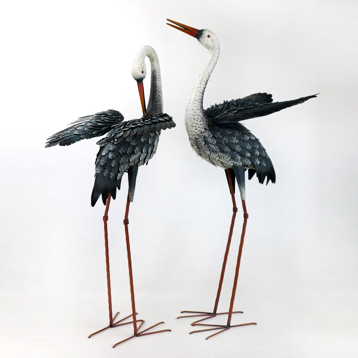 Two metal egret figurines stand side by side with wings spread against a white background.