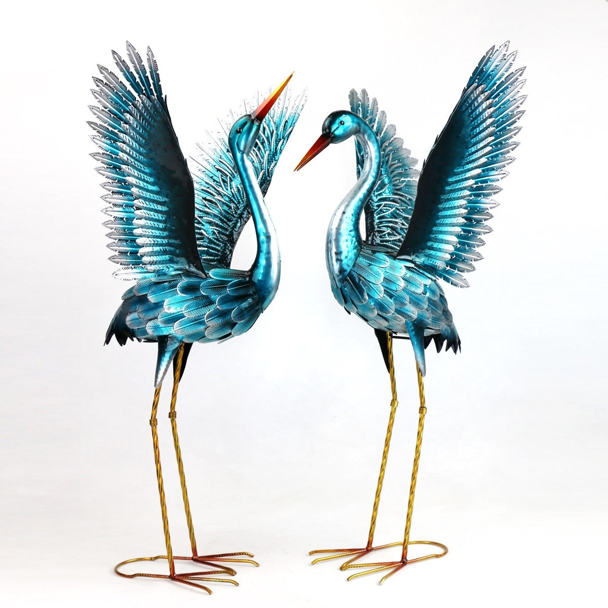 Two blue-green metal crane figurines stand side by side with their wings spread.