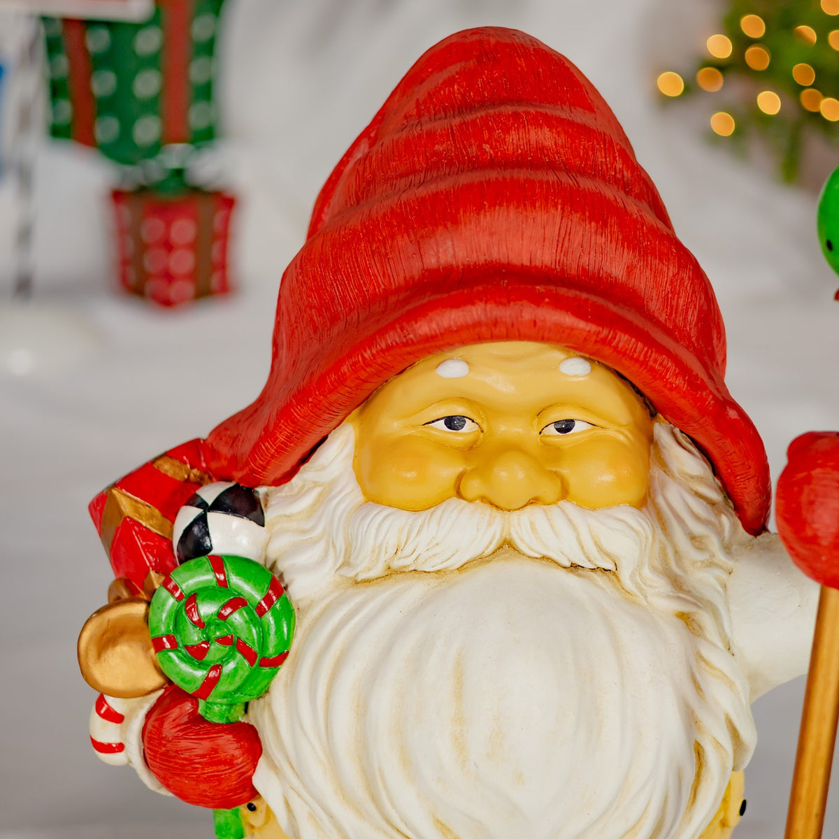 Close view of a red-hatted gnome holding a green lollipop beside its white beard.