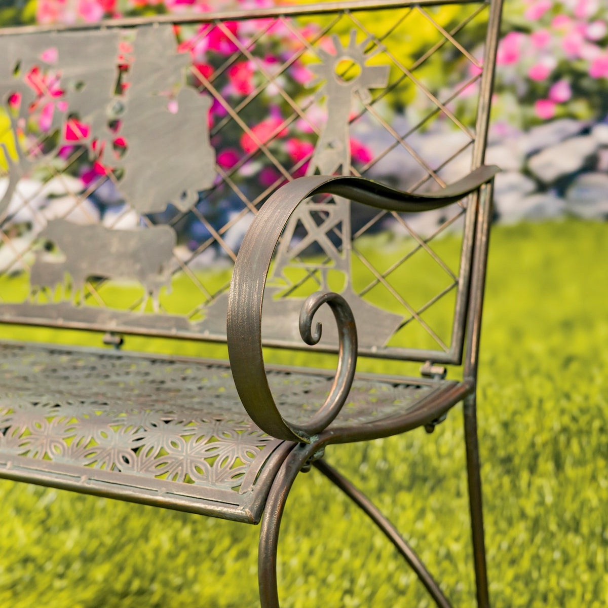 Close view of a curled metal armrest beside the bench’s patterned seat and farm-themed backrest.