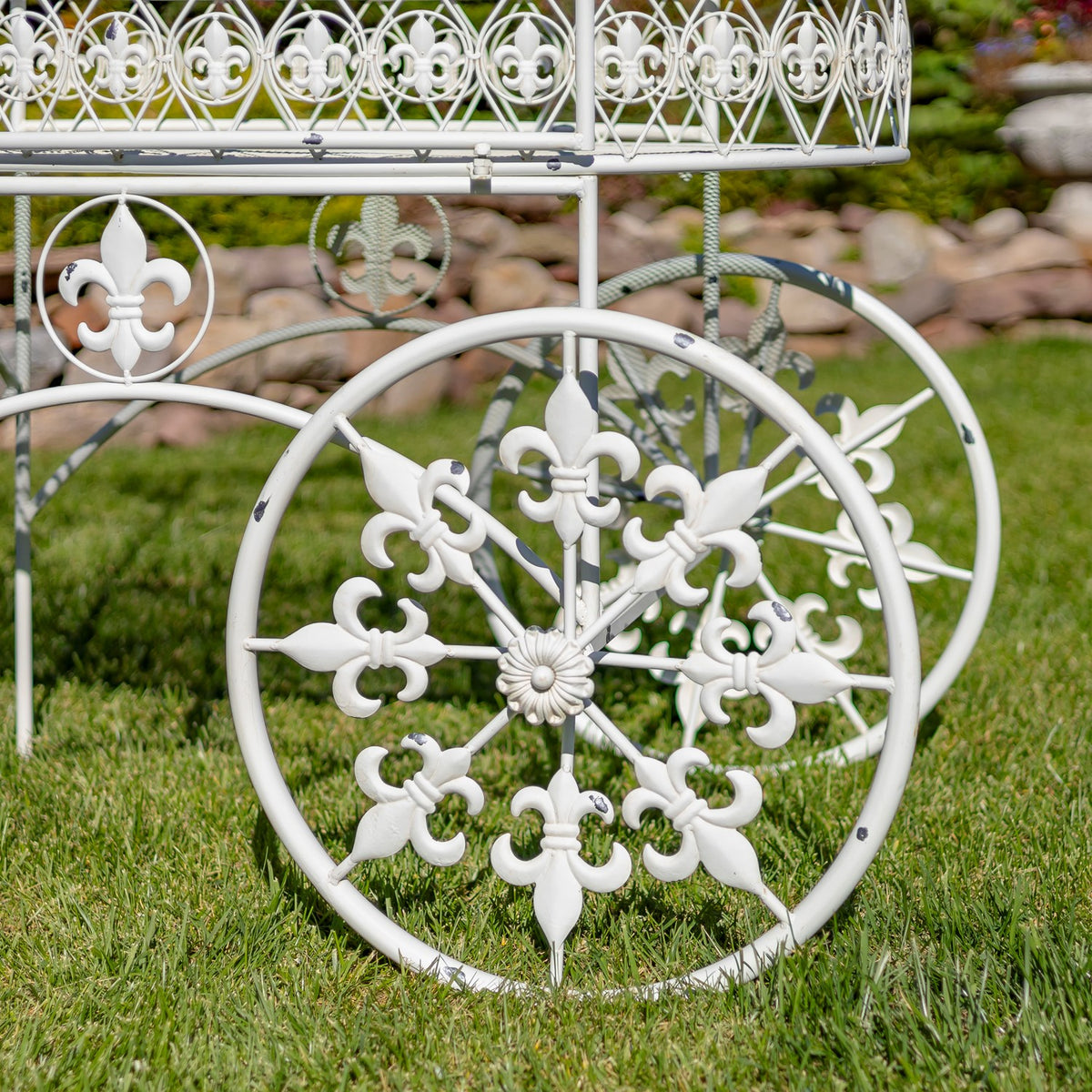 Close-up of an ornate cart wheel with fleur-de-lis spokes and decorative basket railing above.