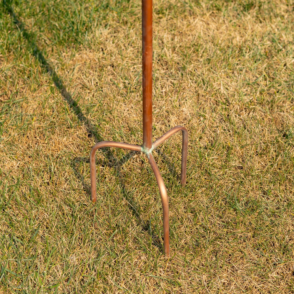 Close-up of the metal stake’s three-pronged base set in grass.
