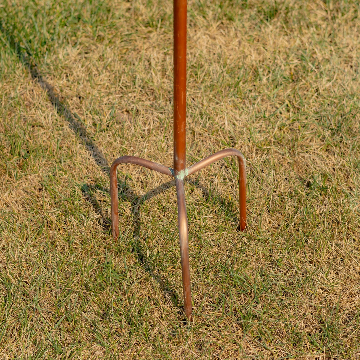 Close-up of the pointed brown stake and curved support legs standing in grass.