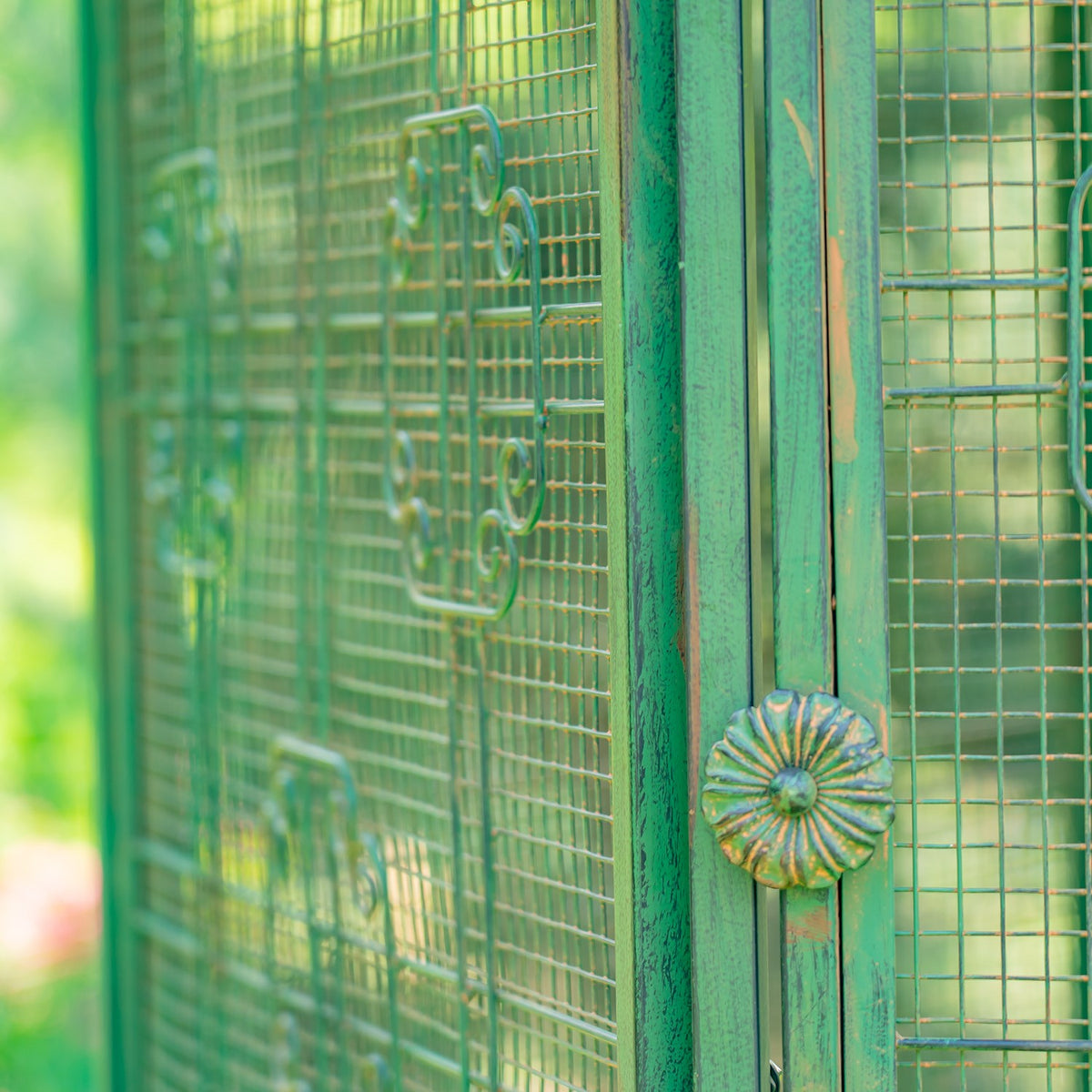 Close-up of a flower-shaped metal latch on a green frame beside mesh panels.