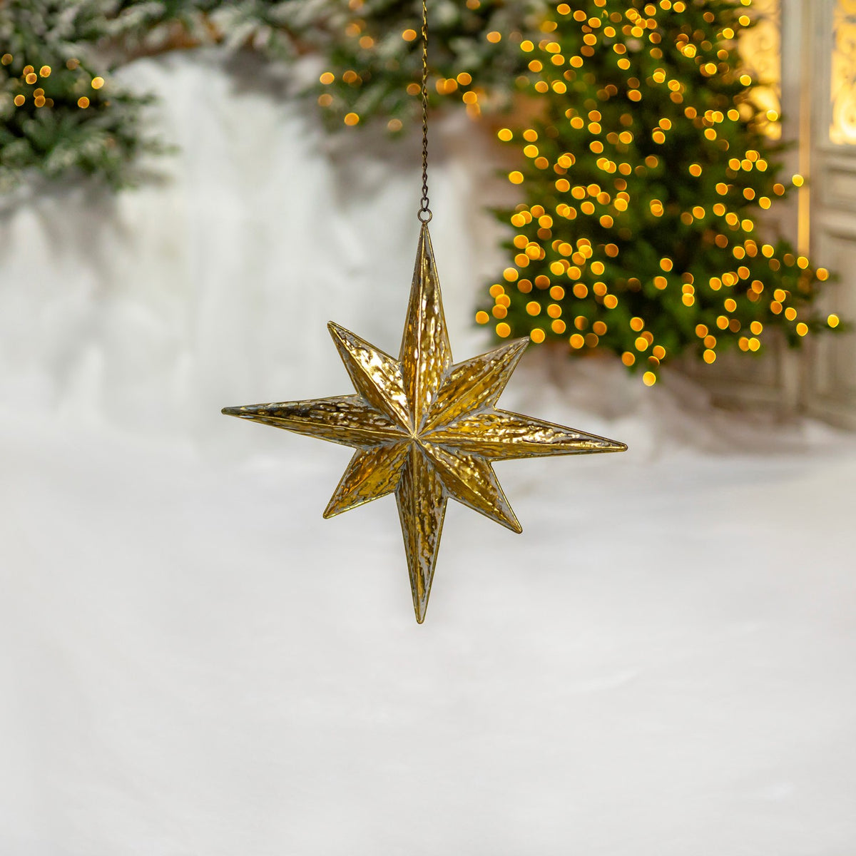 Gold star ornament shown at an angle in front of a glowing Christmas tree.