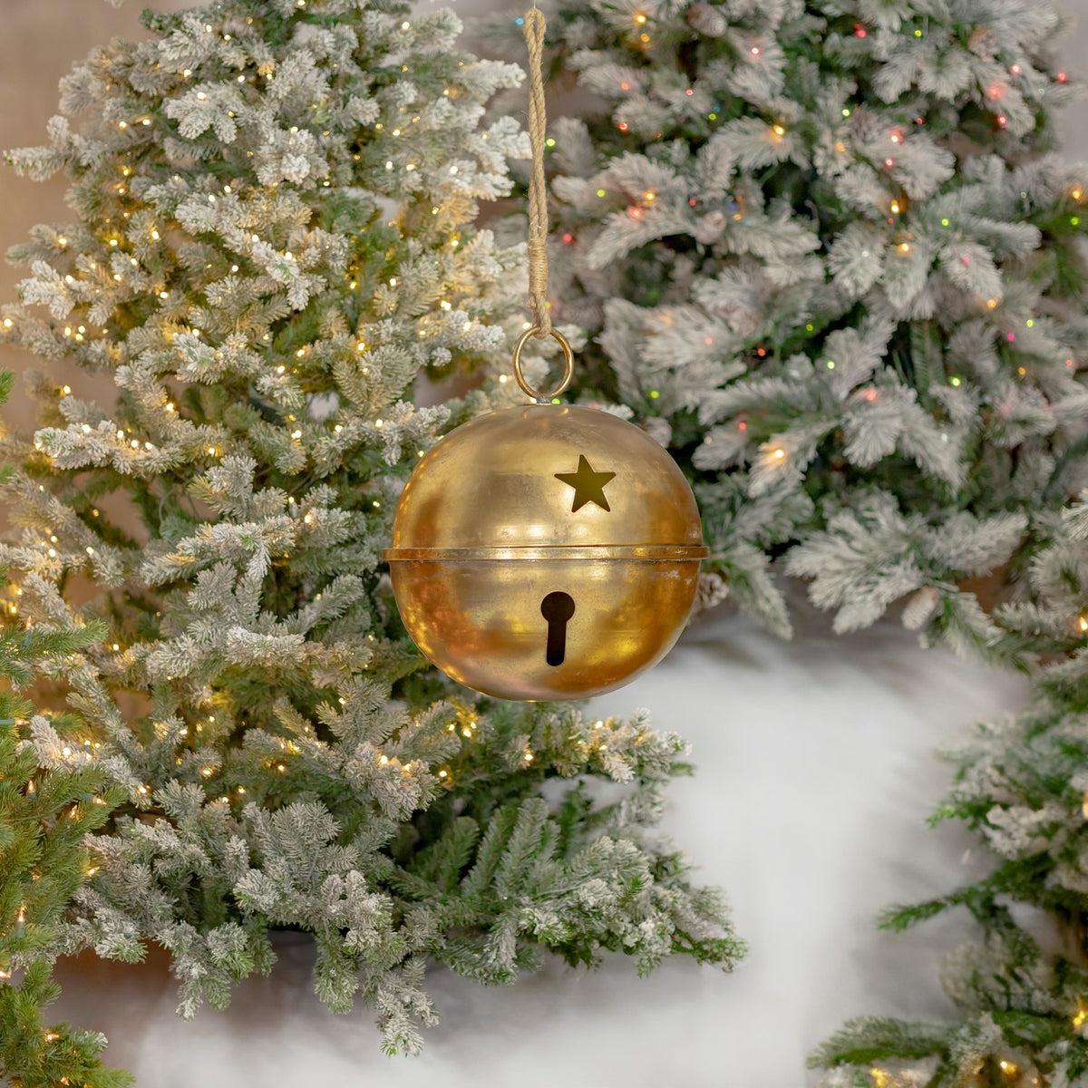 A gold bell with a hanging ring and star cutout hangs against a flocked, lighted Christmas tree.