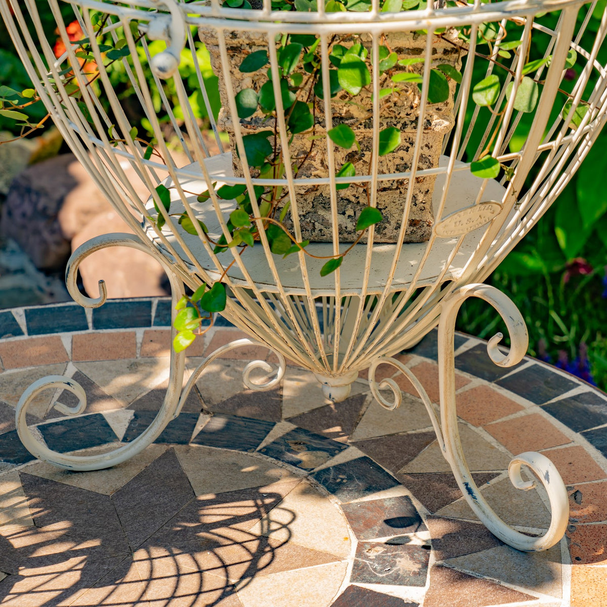 Lower wire frame and scroll feet surrounding a potted plant on a tiled table.