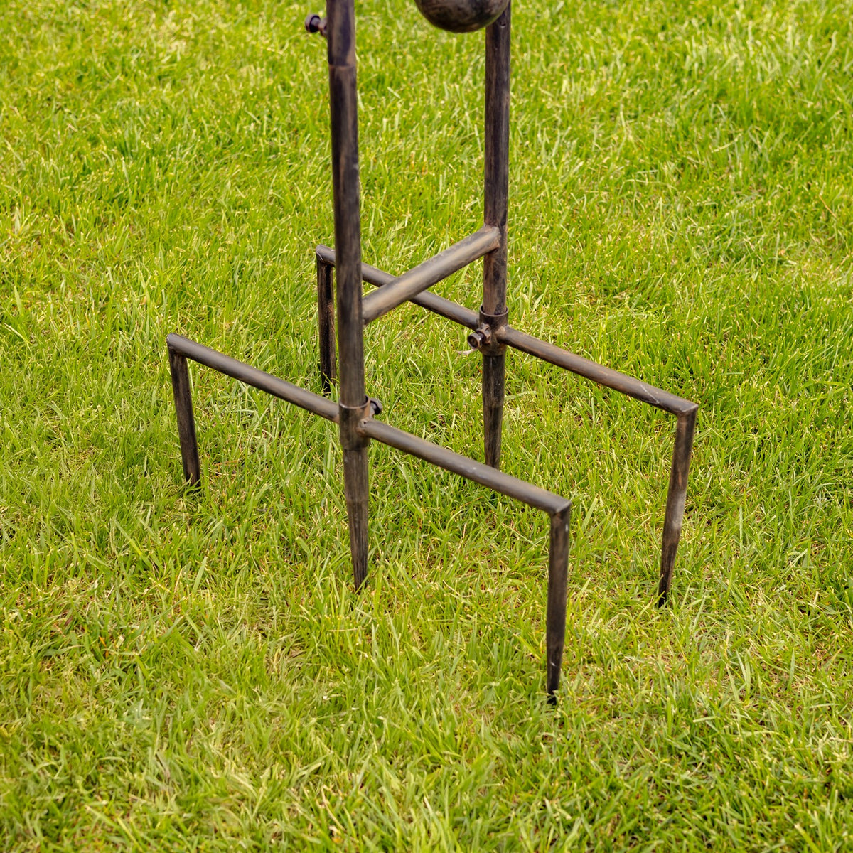 Dark metal garden stake legs planted in green grass, with the upper ornament cropped out of view.