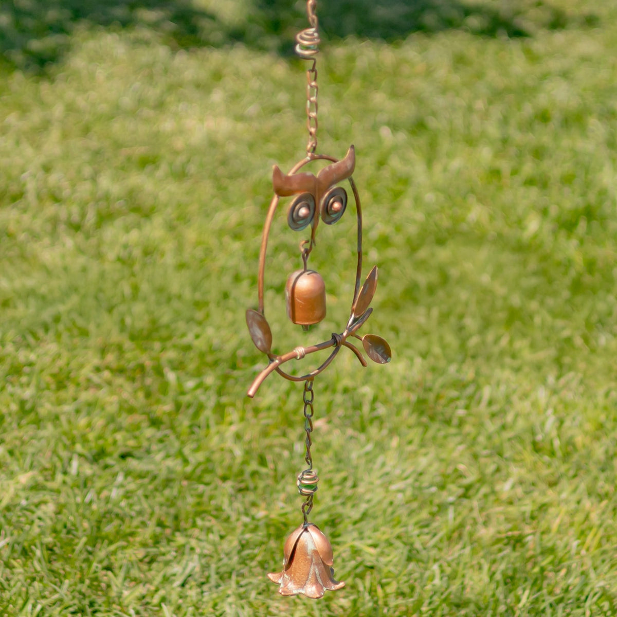 Owl rain chain suspended over grass, with linked chain sections and a flower-shaped bell below.