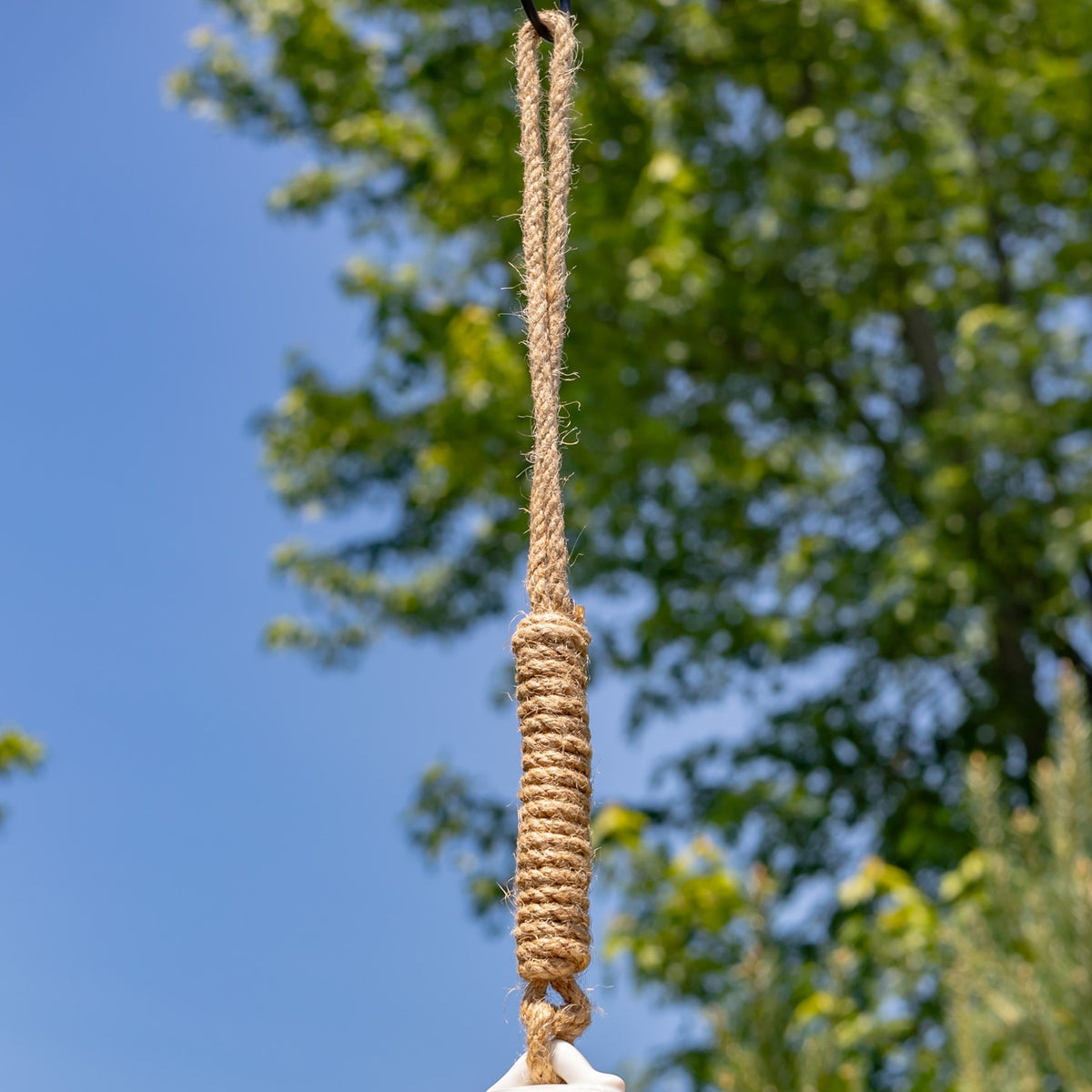 Close-up of the coarse twisted hanging rope and its wrapped section against blue sky and leafy branches.