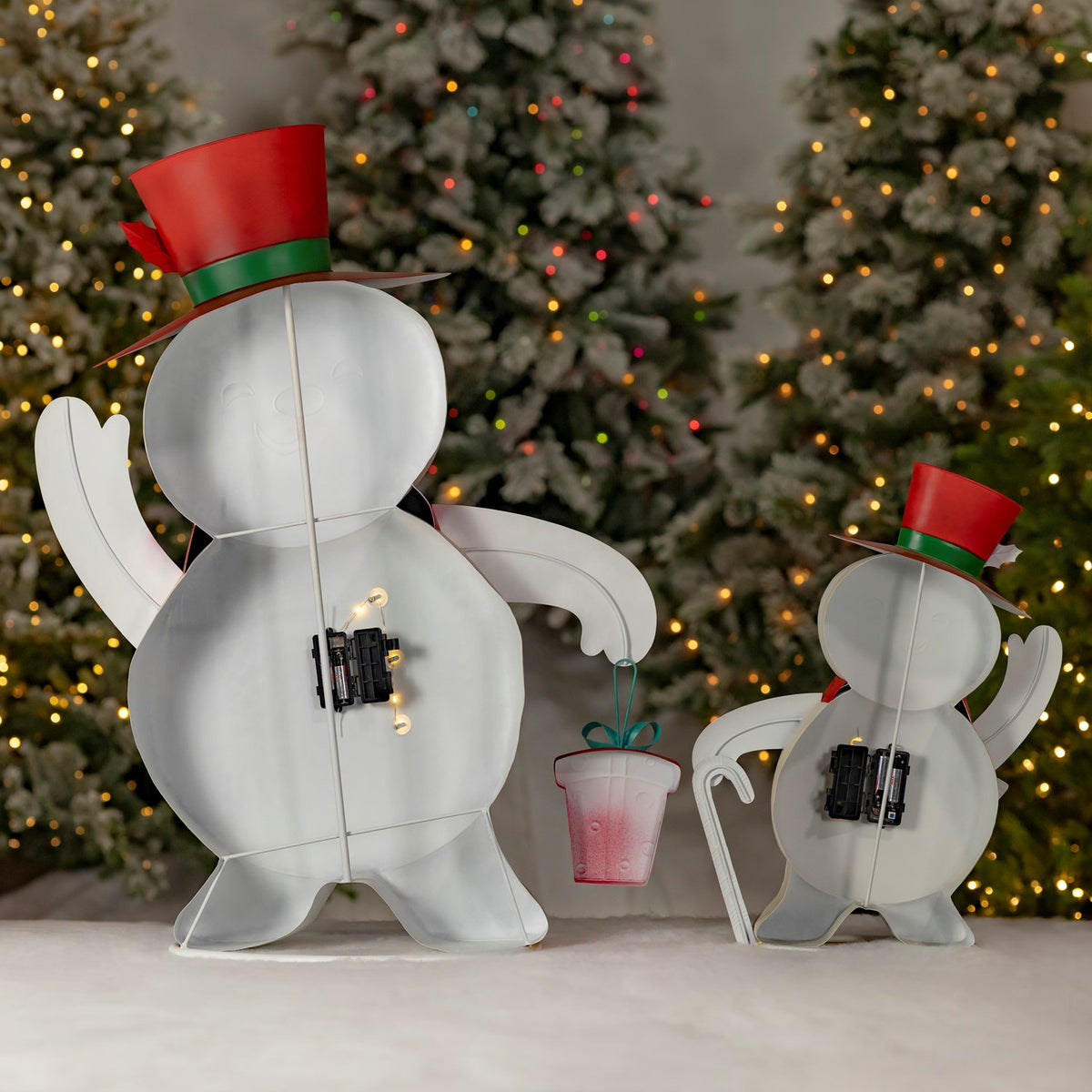 Backs of two snowman figurines showing their hats, raised arms, and attached battery packs.