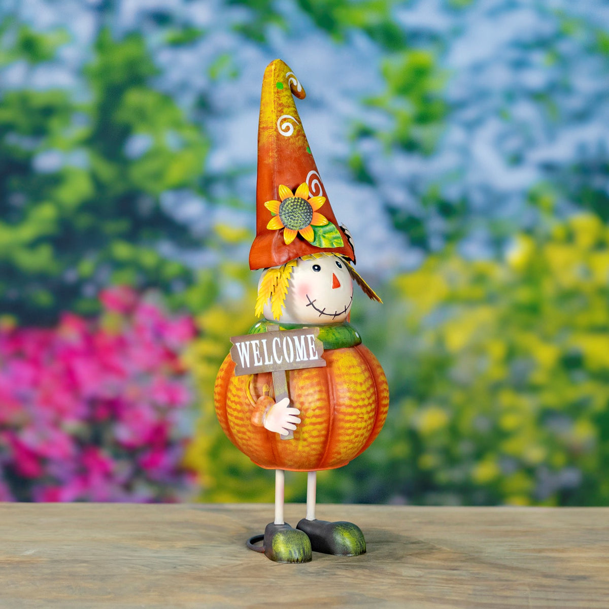 Pumpkin scarecrow with a curled orange hat, yellow hair, and a small sign stands on a wooden surface.