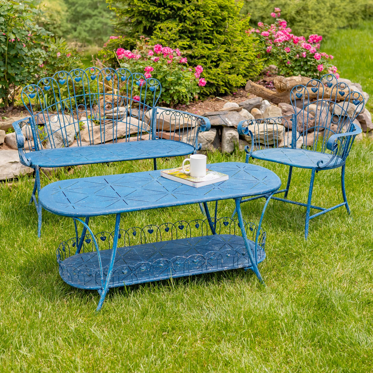 Blue wrought-iron bench and matching chairs arranged around a low table on a lawn among flowering plants.