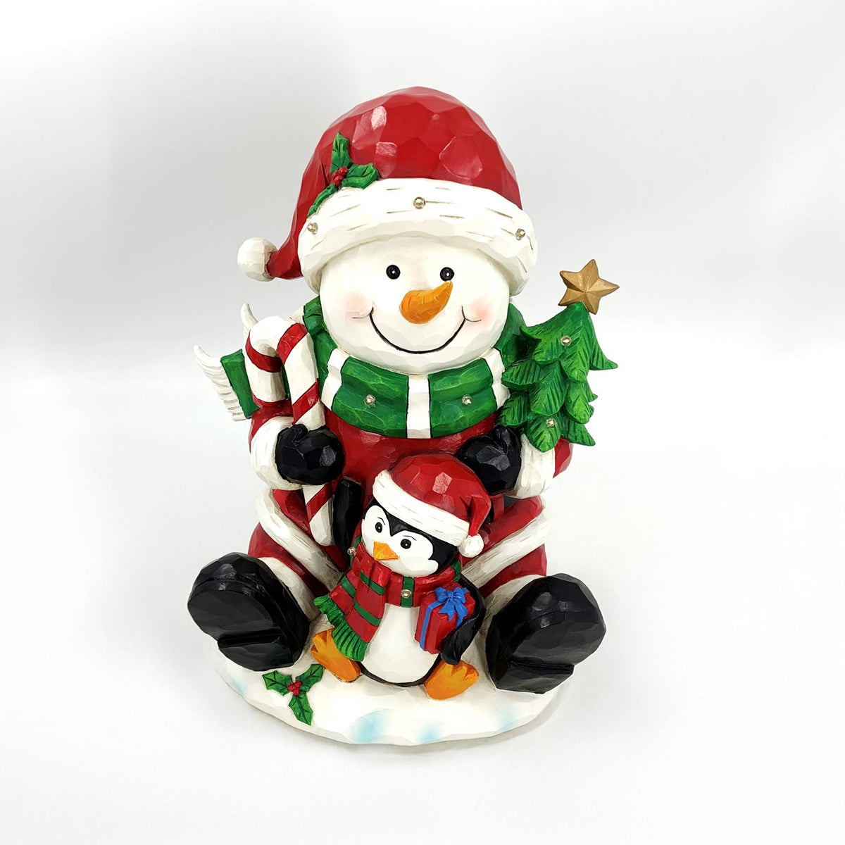 Snowman and penguin sit together in festive outfits, with a candy cane and decorated Christmas tree.