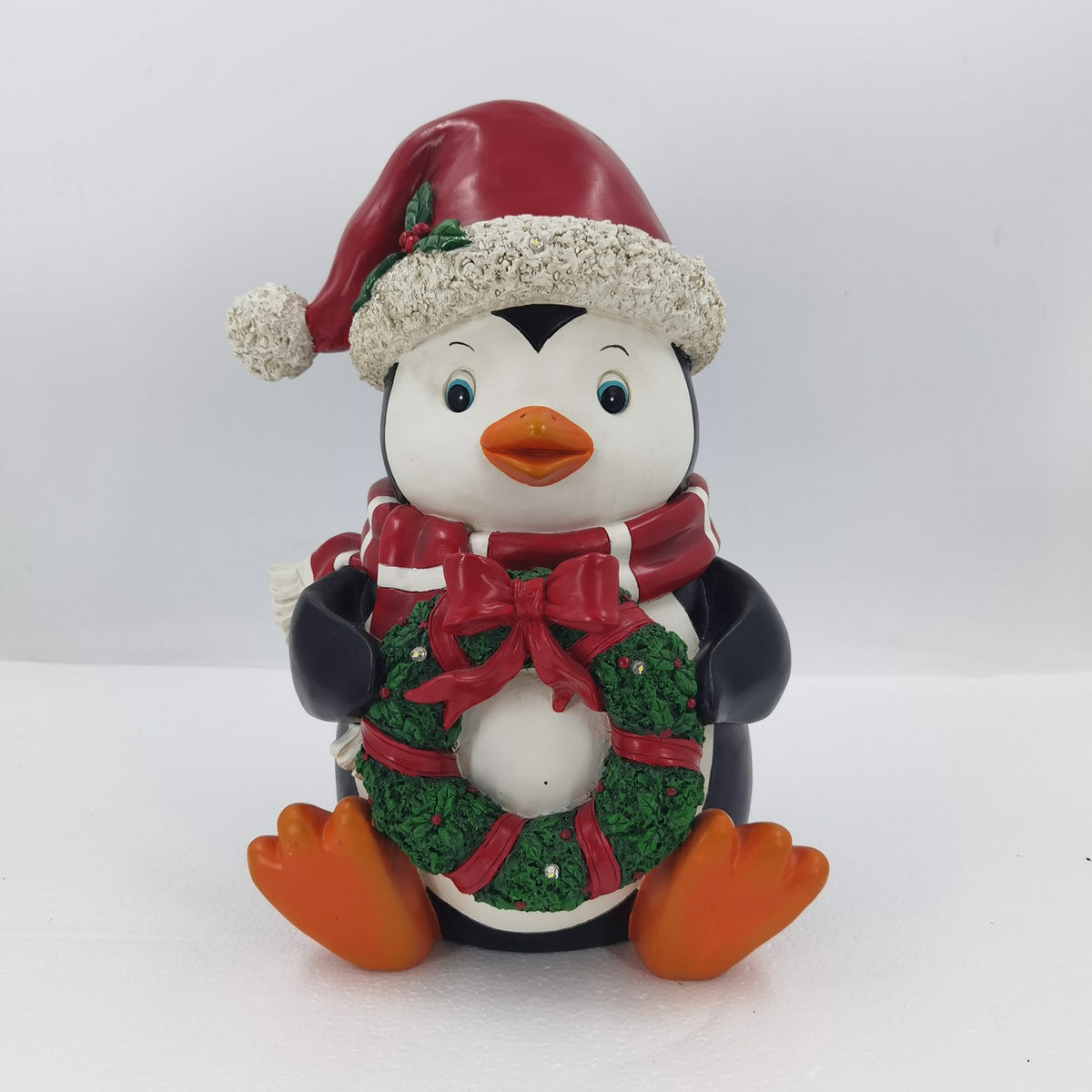 Full view of the seated penguin holding a green wreath decorated with red ribbons and a bow.