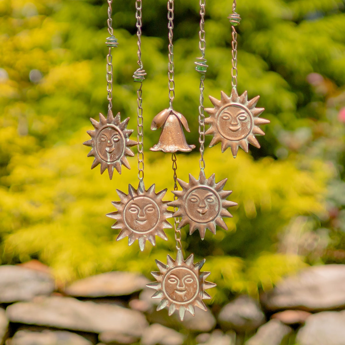 Close-up of several smiling sun pendants and a bell suspended from chains beneath the moon.