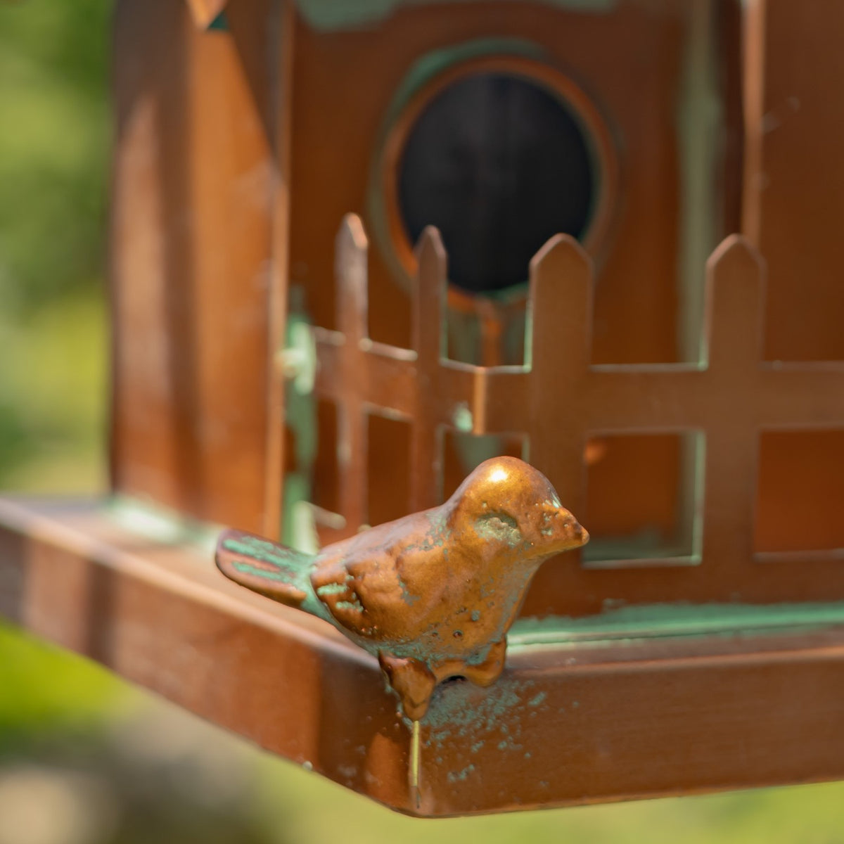 Close-up of a small metal bird ornament perched on the birdhouse's copper-colored base.