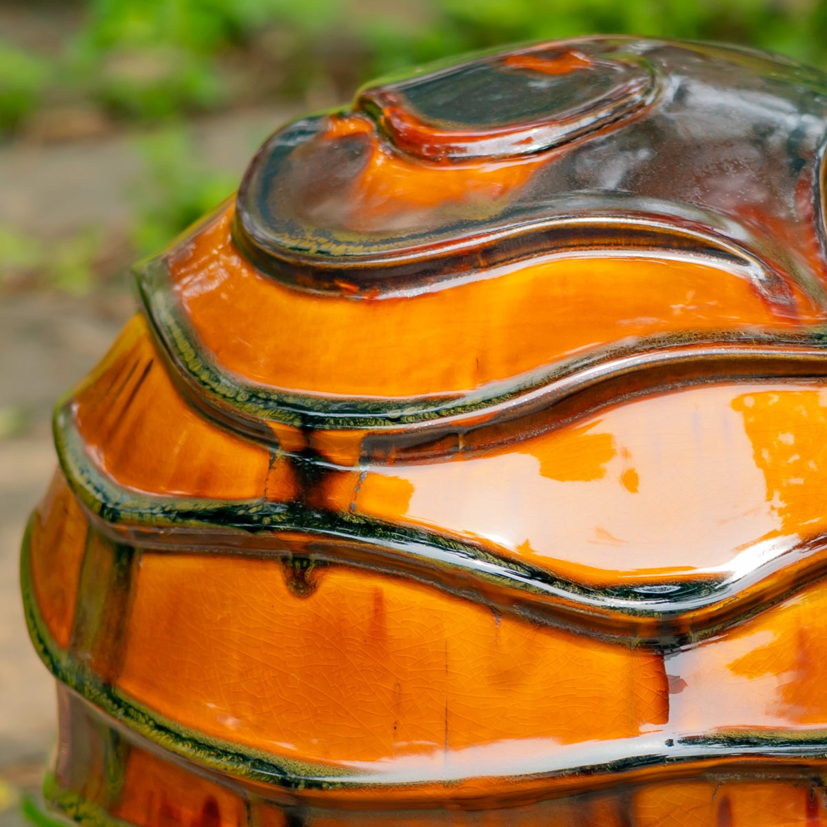 Close-up of glossy orange glaze, dark wavy ridges, and irregular brown accents on a globe.