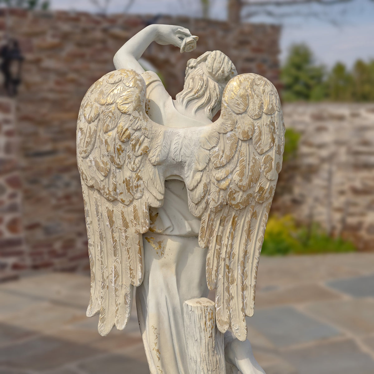 Back view of the angel statue, showing its raised arm and long, carved wings.