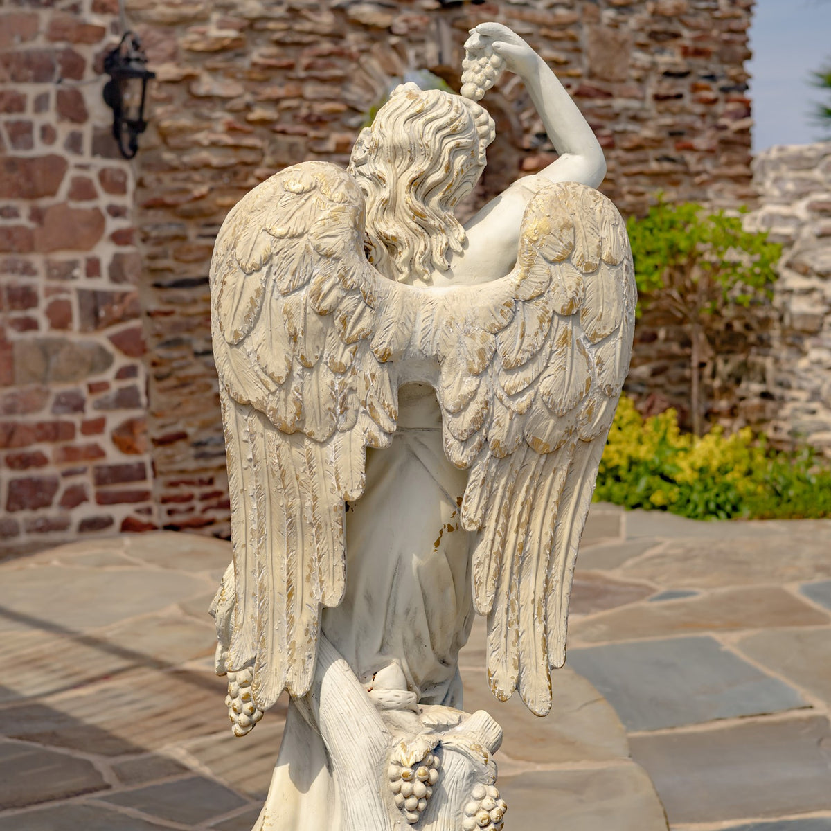 Back of the angel statue showing its long feathered wings and raised arm.