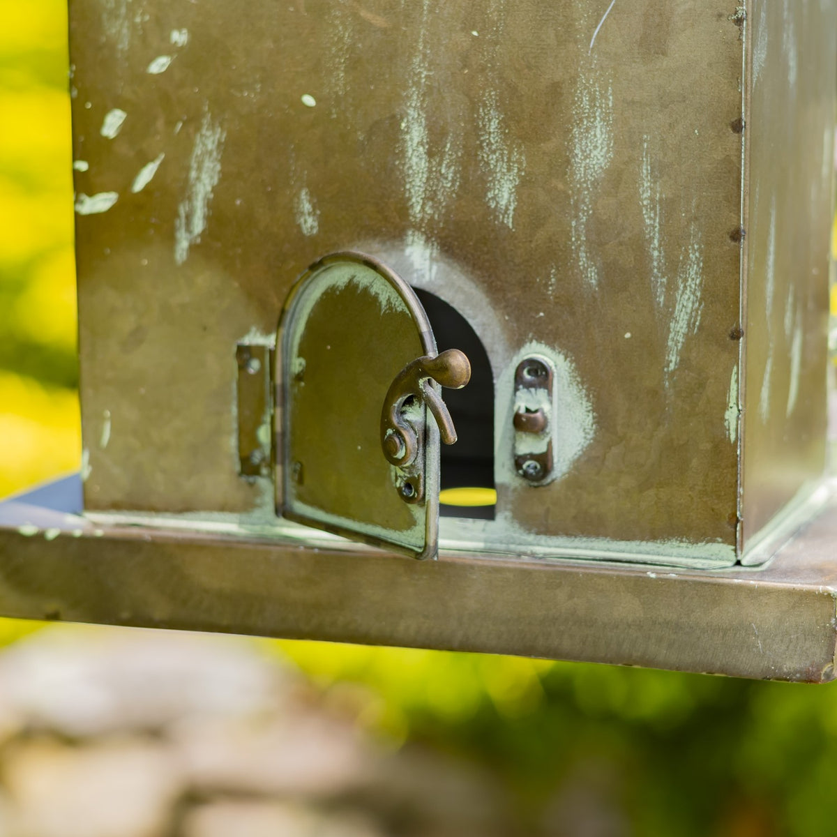 Close-up of a small arched metal door and latch on the weathered birdhouse wall.