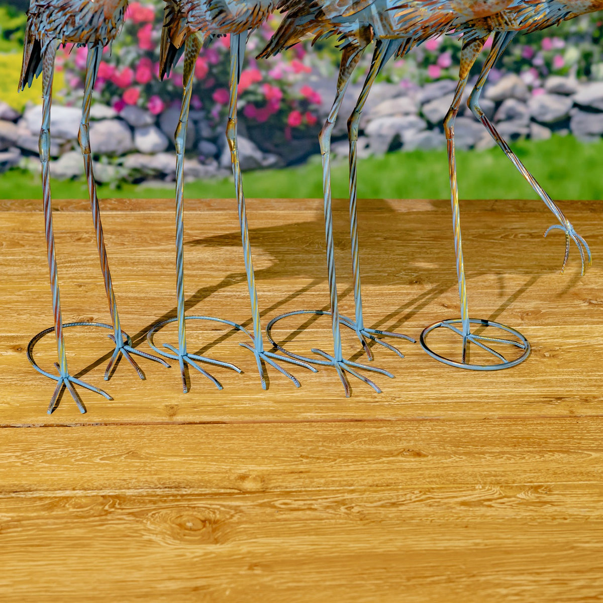 Lower portions of several metal heron figurines show long legs and varied wire feet on a wooden surface.