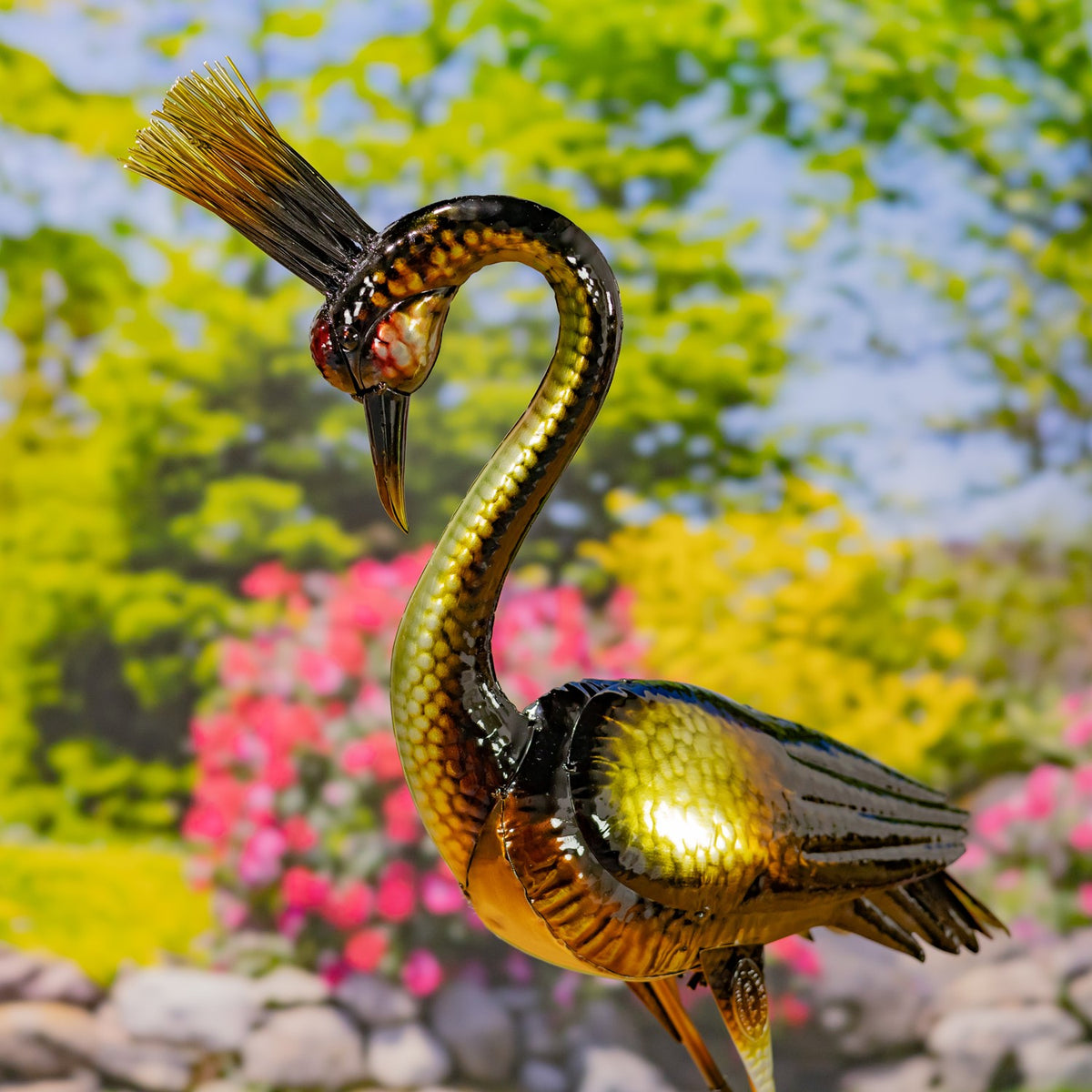 Side view of a metallic heron figurine with a long curved neck and layered dark wings.