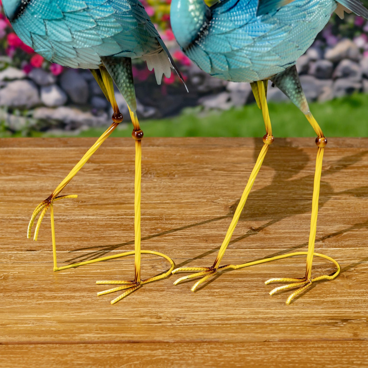 Close-up of the figurines’ long yellow legs and curled metal feet on a wooden surface.