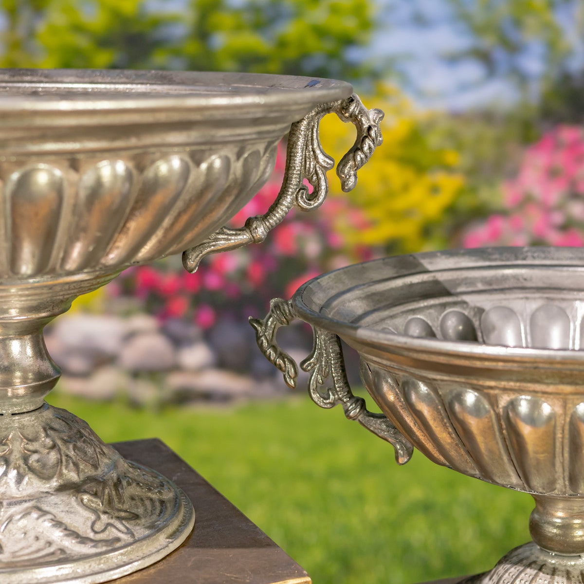 Close-up of two silver urns showing their fluted bowls and curled decorative handles.