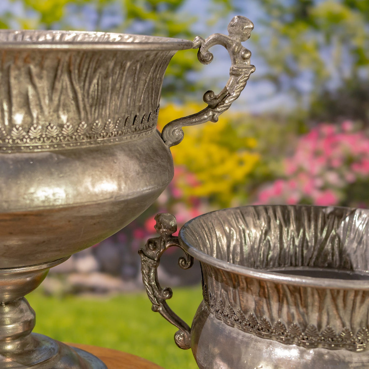 Close-up of ornate handles and fluted rims on two frosted silver urns.