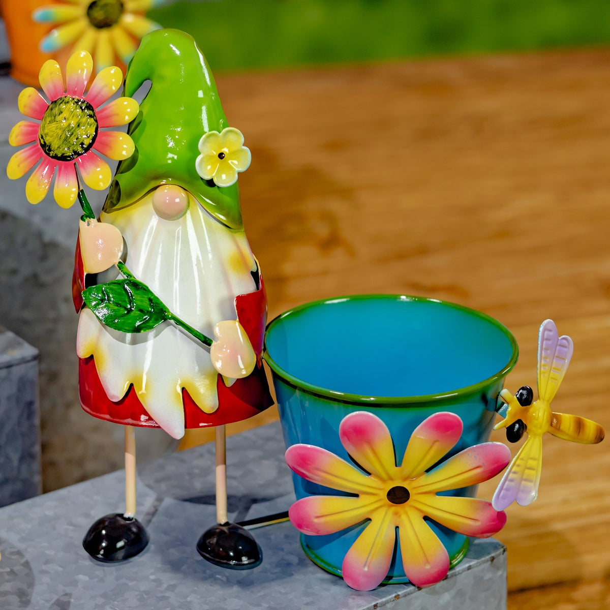 A green-hatted gnome stands beside a blue pot with a large yellow-pink flower and dragonfly.