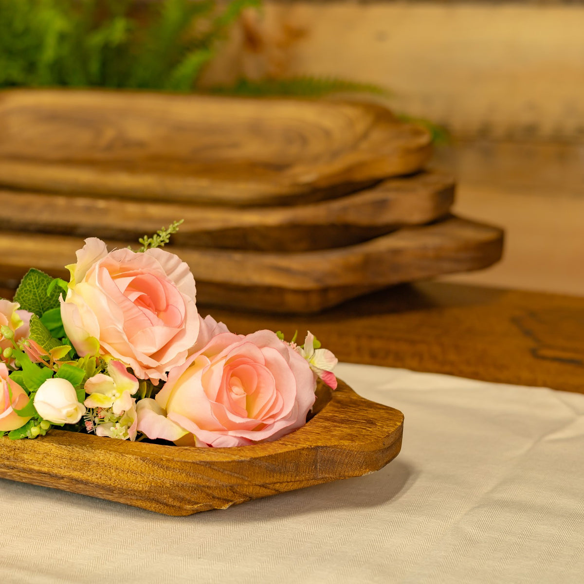 A wooden tray with pink roses sits in the foreground beside a stack of trays.