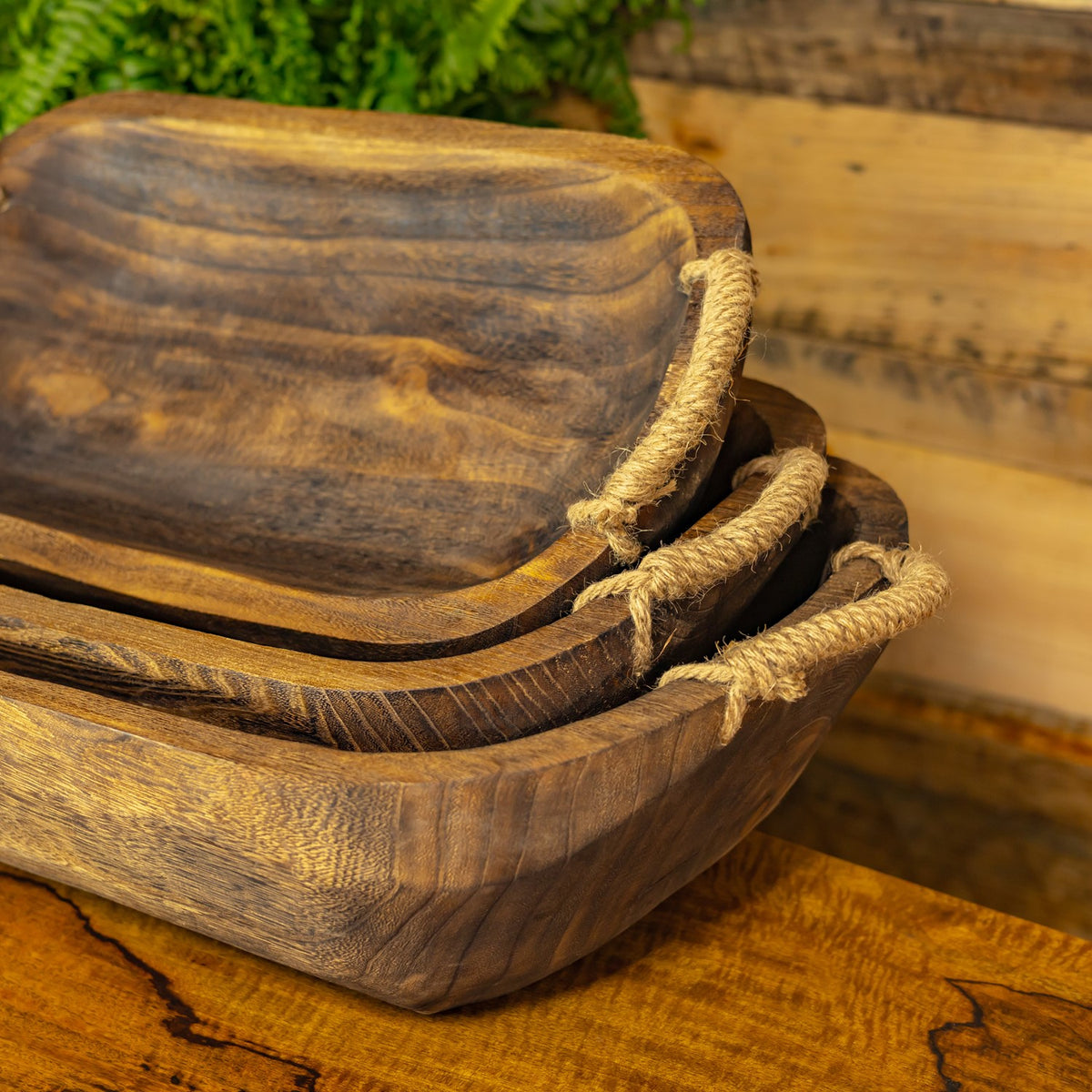Close view of nested wooden trays showing their textured grain and thick rope handles.
