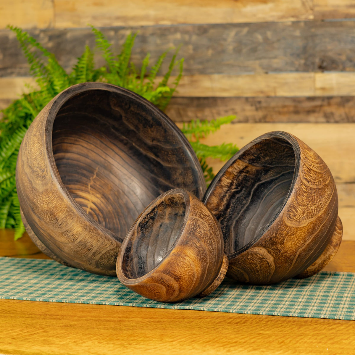 Three empty round wooden planters in graduated sizes arranged together on a checked cloth.