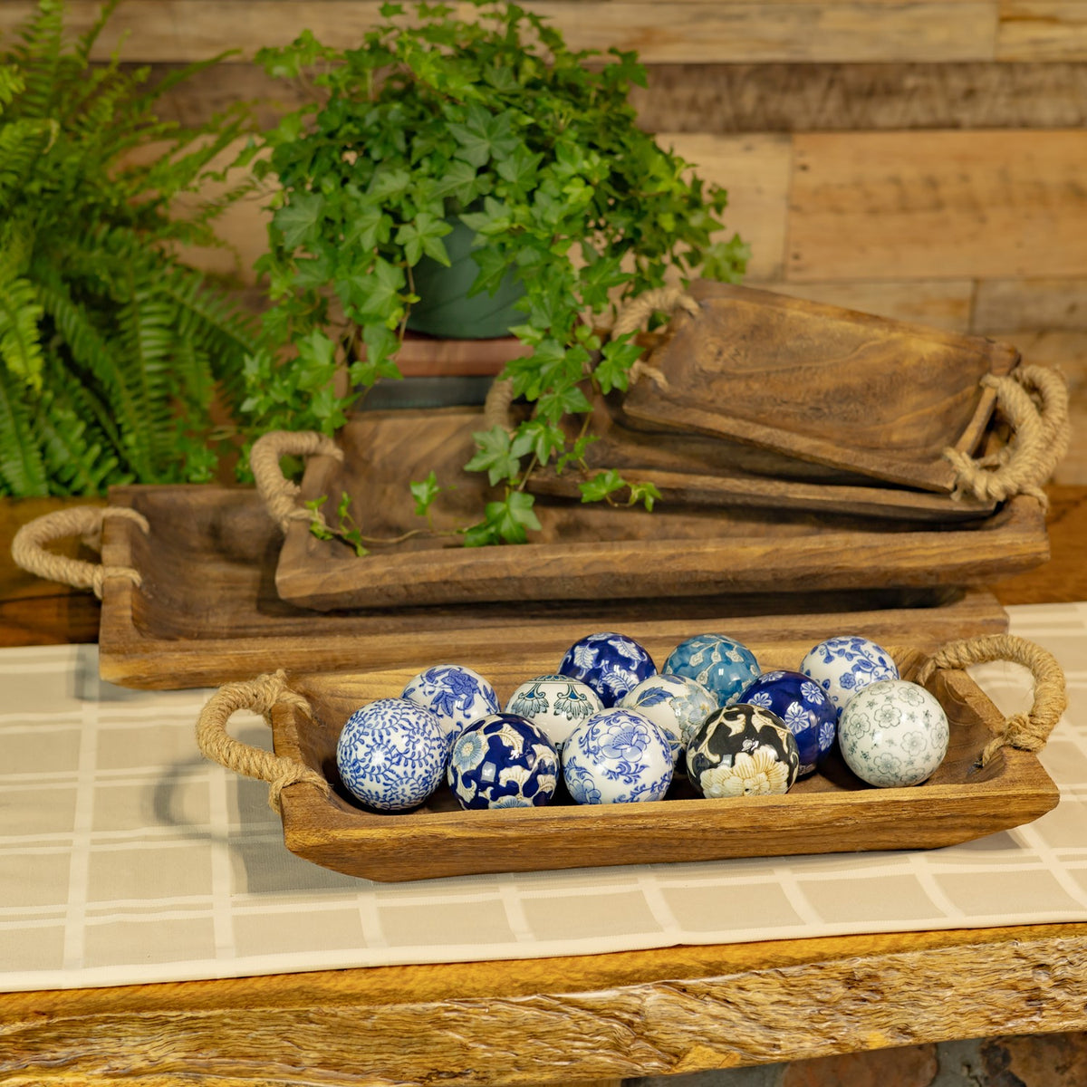 Three wooden trays with rope handles hold decorative blue and white patterned spheres.