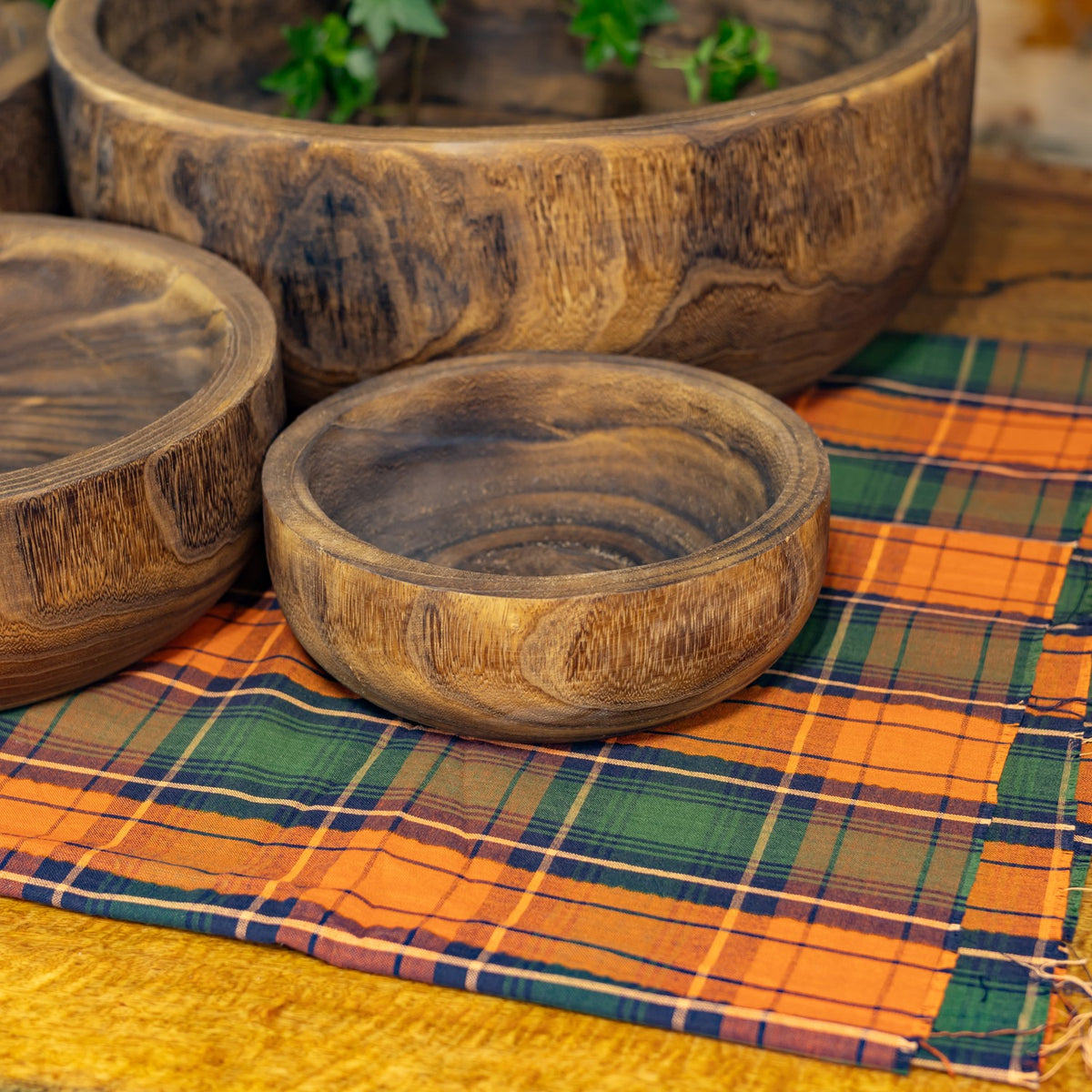 Three round wooden bowls of varying sizes displayed on plaid fabric, showing their carved interiors and grain.