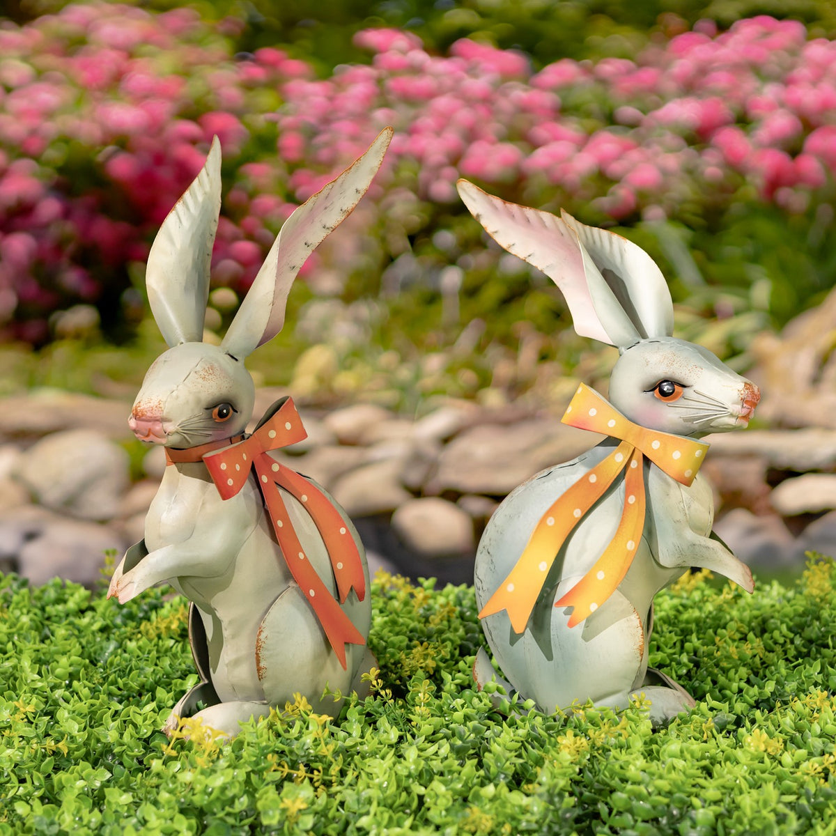 Two seated pale metal rabbit figurines with tall ears and contrasting orange and yellow polka-dot ribbons.