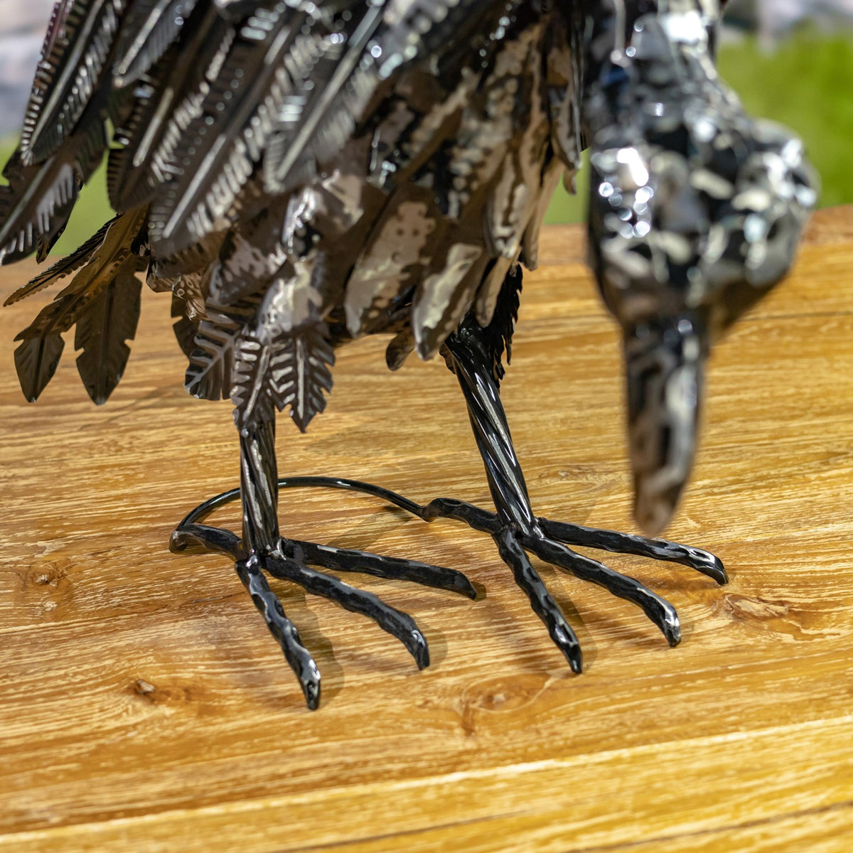 Close-up of two dark metallic bird figurines’ textured legs and clawed feet on a wood surface.