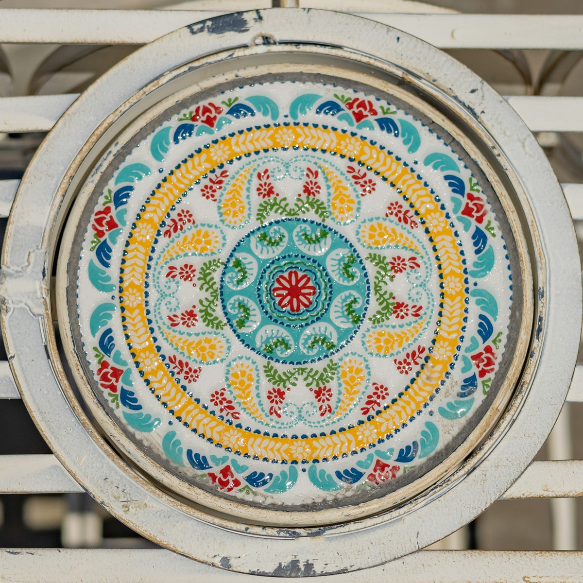 Round tabletop with a colorful, intricate floral mosaic framed by distressed ivory metal.