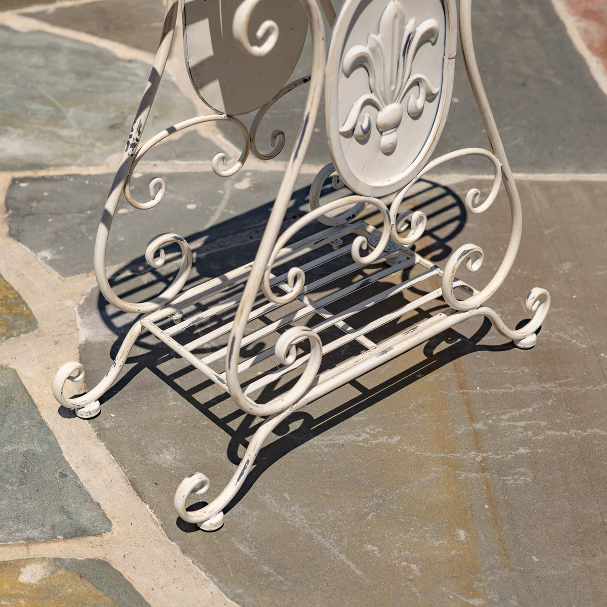 Close angled view of the stand’s curled metal feet, lower slatted shelf, and raised decorative panel.
