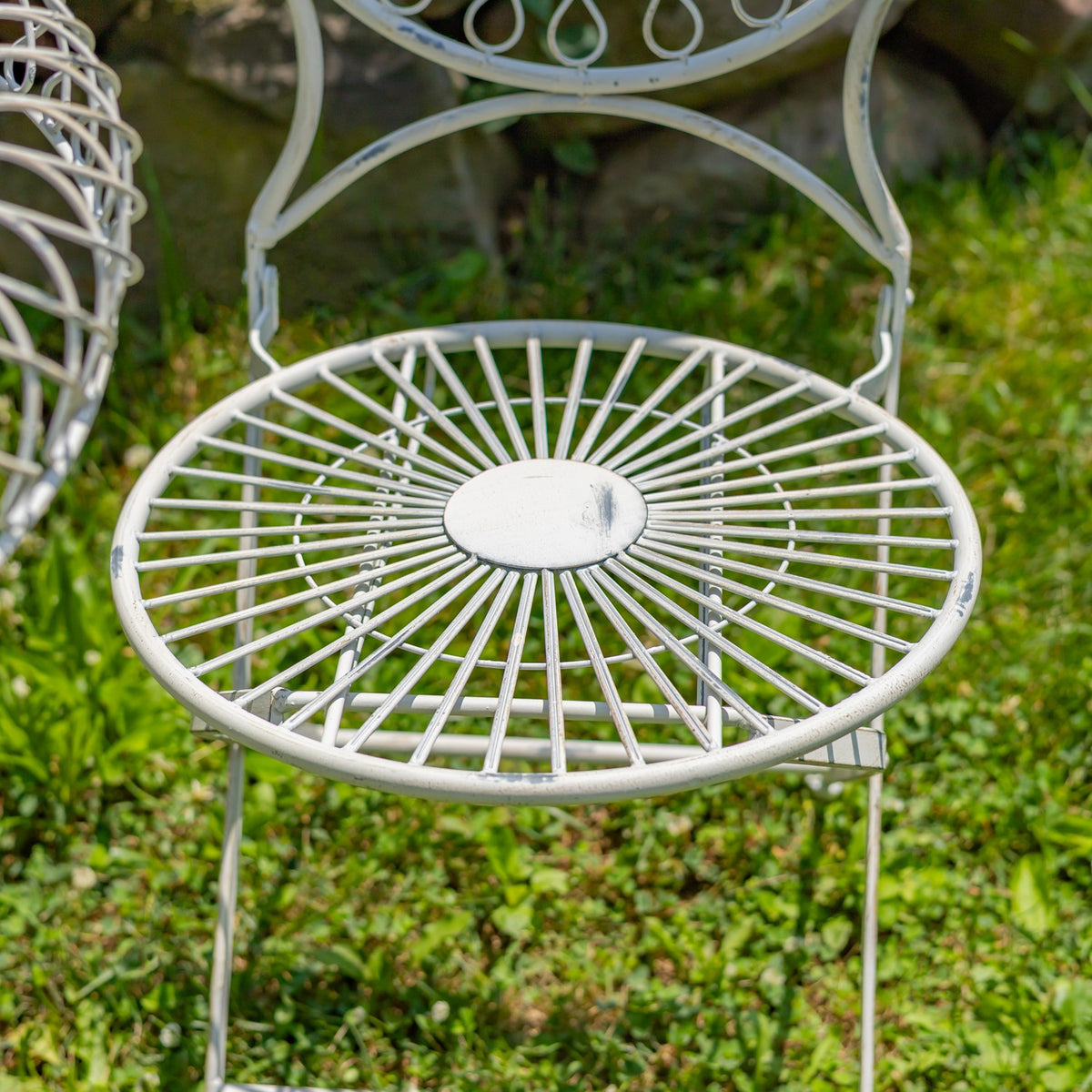 Close-up of a white wire-frame chair seat with radial spokes and a circular center plate, outdoors on grass.