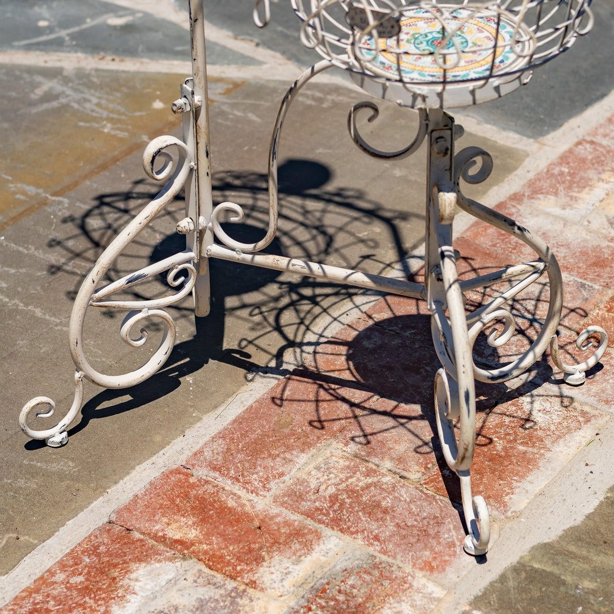 Close-up of the stand's curled metal legs, feet and central support on a stone patio.